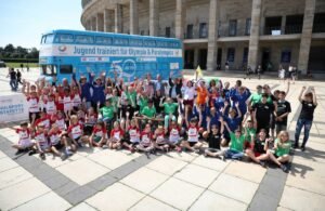 Gruppenfoto zur Veranstaltung Schulsport-Stafette 2021 vor dem Jugend trainiert für Olympia Bus. Olympiastadion Berlin im Hintergrund