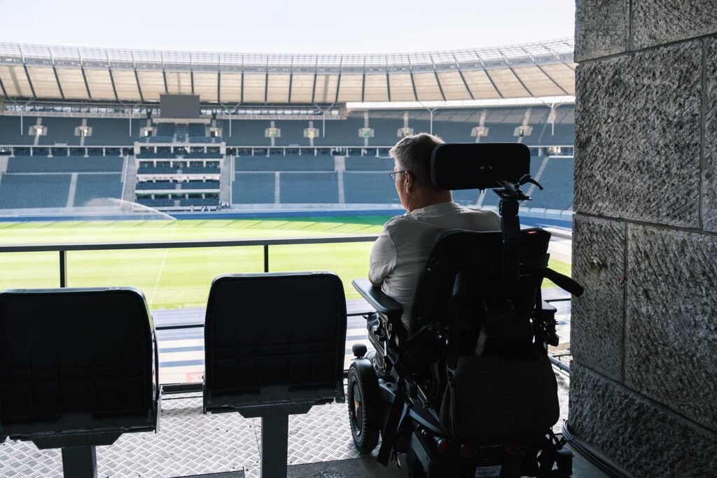 Ein Mann im elektrischen Rollstuhl blickt von einer barrierefreien Zuschauerplattform auf das Spielfeld und die Ränge des leeren Olympiastadions Berlin.