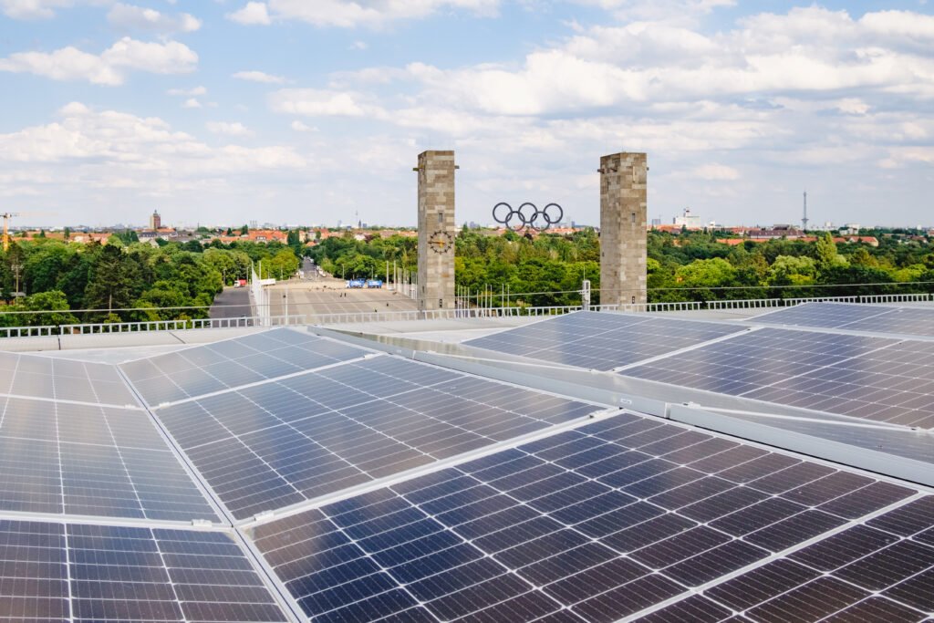 Photovoltaikanlage auf dem Dach des Olympiastadions Berlin mit Blick auf die historischen Türme des Osttors samt Olympischen Ringen und der umgebenden Stadtlandschaft.