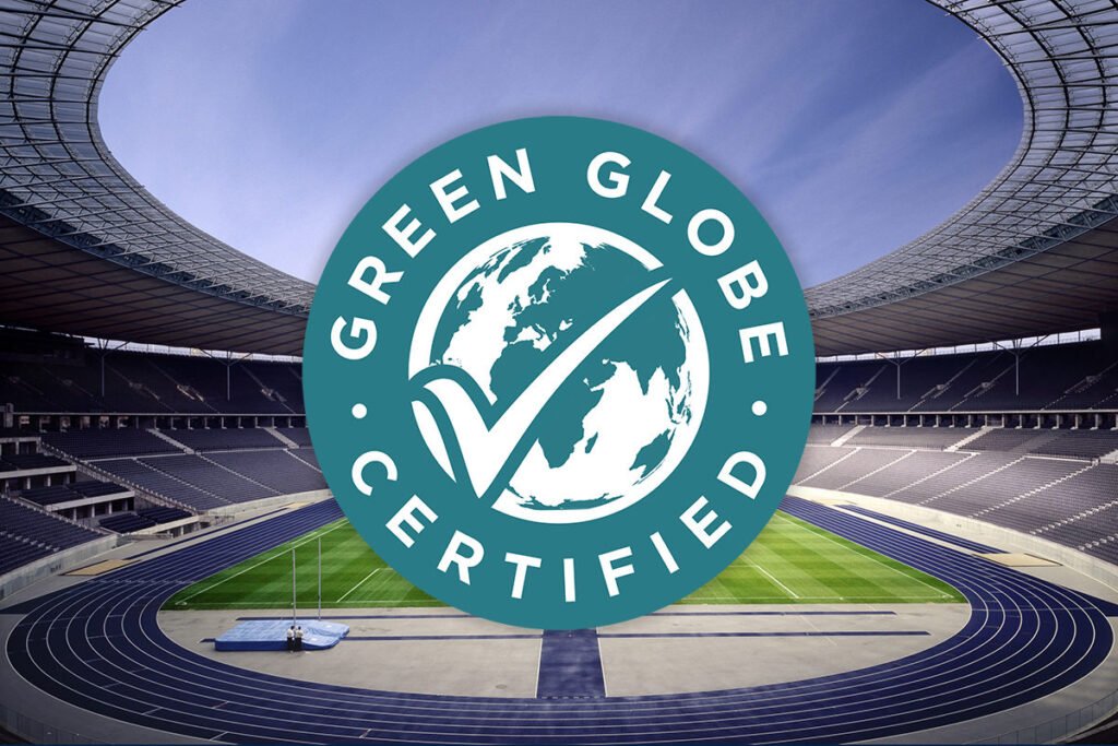 Das türkis-weiße Logo „GREEN GLOBE CERTIFIED“ ist zentral über eine Innenansicht des Olympiastadions Berlin mit seiner blauen Laufbahn und dem Rasenplatz gelegt.
